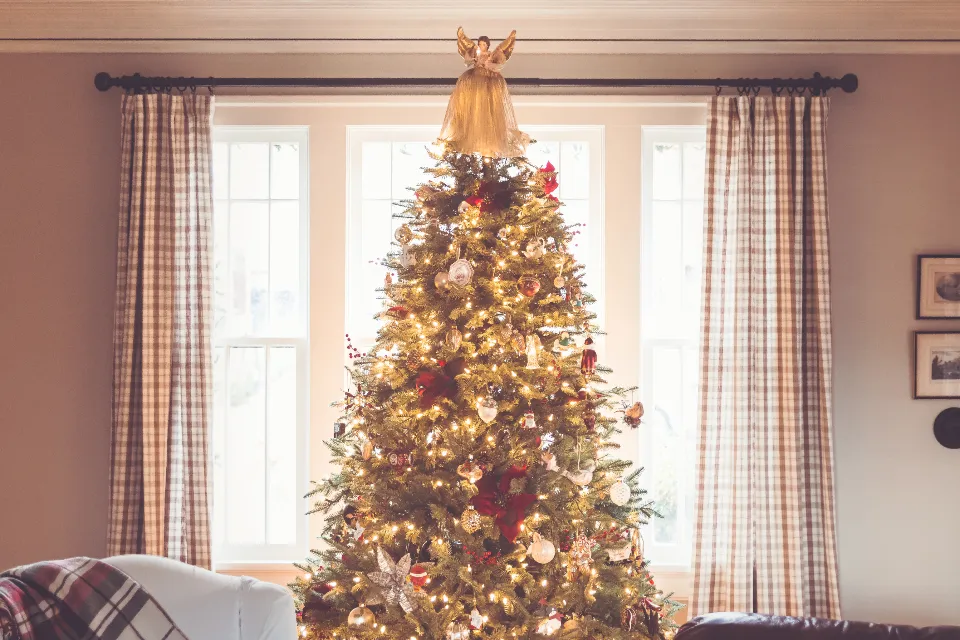 Árbol de Navidad iluminado junto a una ventana, en un salón con luz cálida