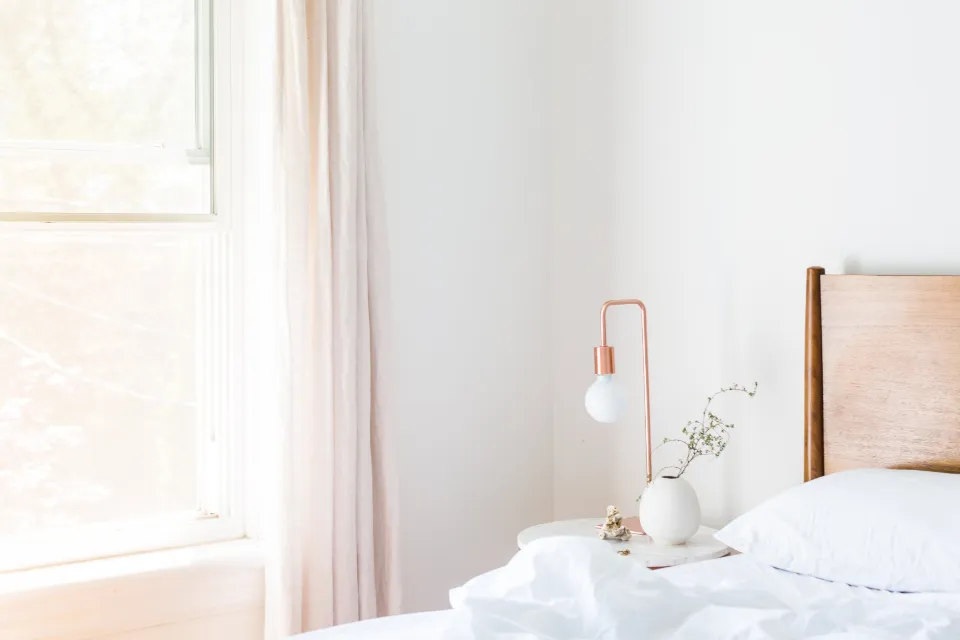Dormitorio con sábanas blancas, una lámpara de cobre y luz suave entrando por la ventana