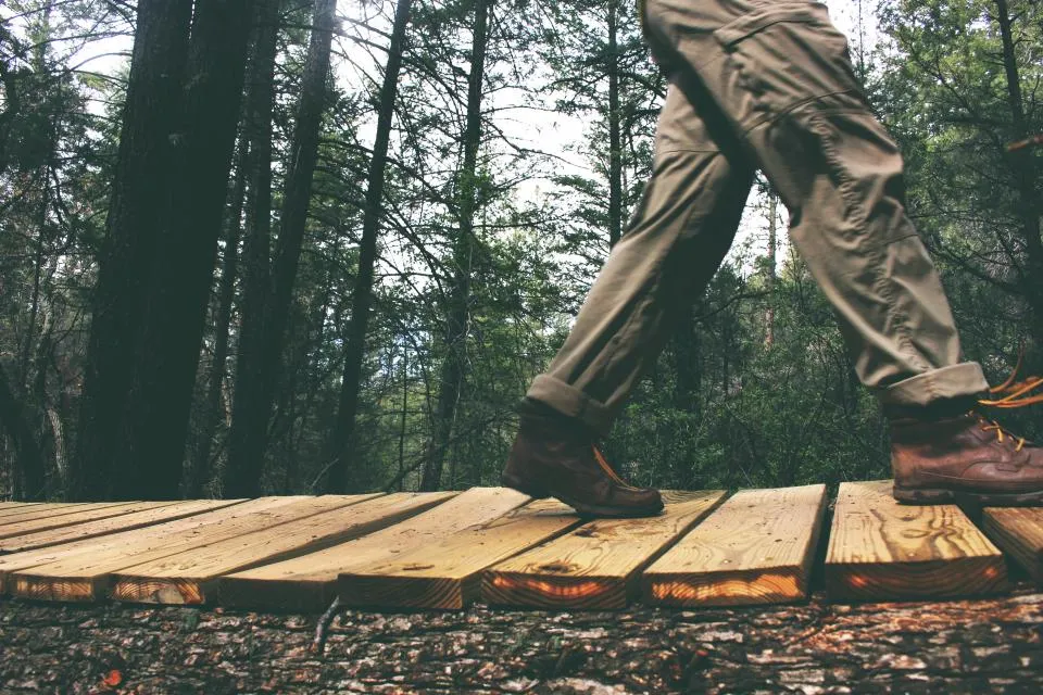 Piernas de una persona caminando por una pasarela de madera en un bosque